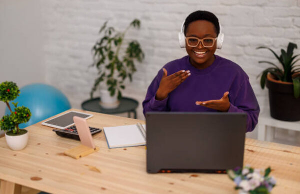 A beautiful young African woman is working from home while using a laptop to communicate with her colleagues via conference call.